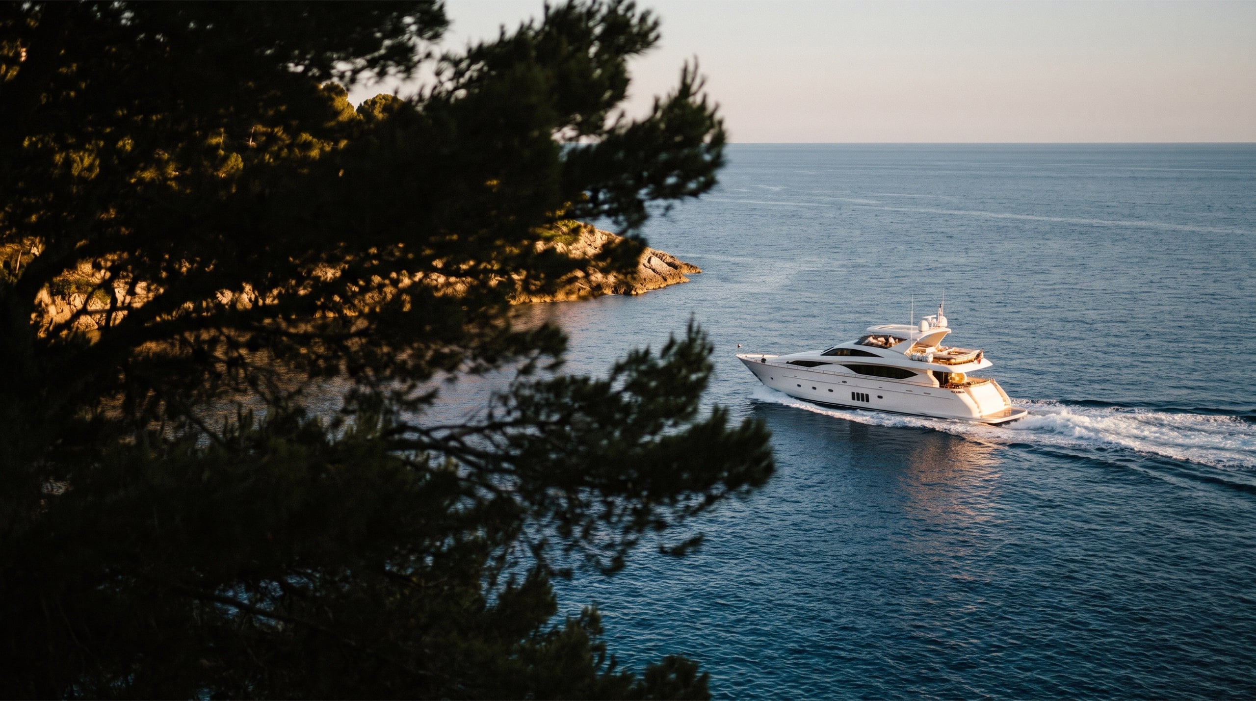 Yacht longeant la côte rocheuse de la Riviera en fin de journée